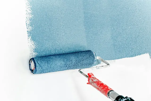 A paint roller rolling blue paint onto a white wall