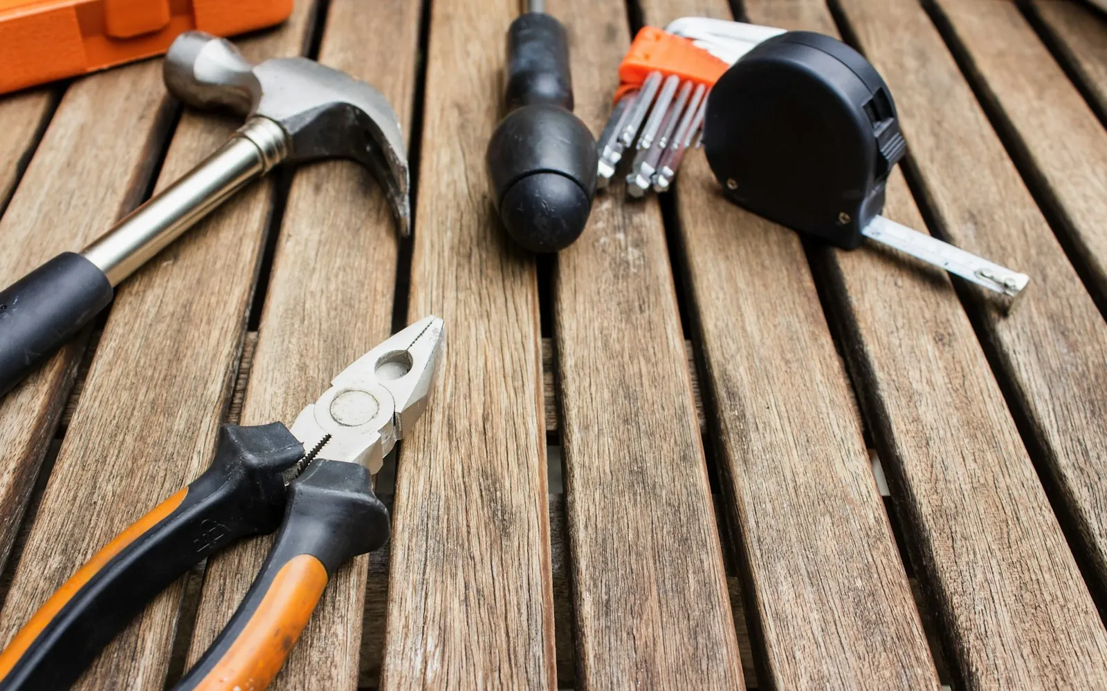 A hammer, pliers, a screwdriver, hex keys and a tape measure laid out on a wooden deck