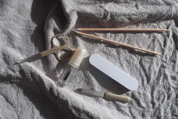 Nail scissors, wooden sticks, a nail file and a buffer laid out on a grey towel